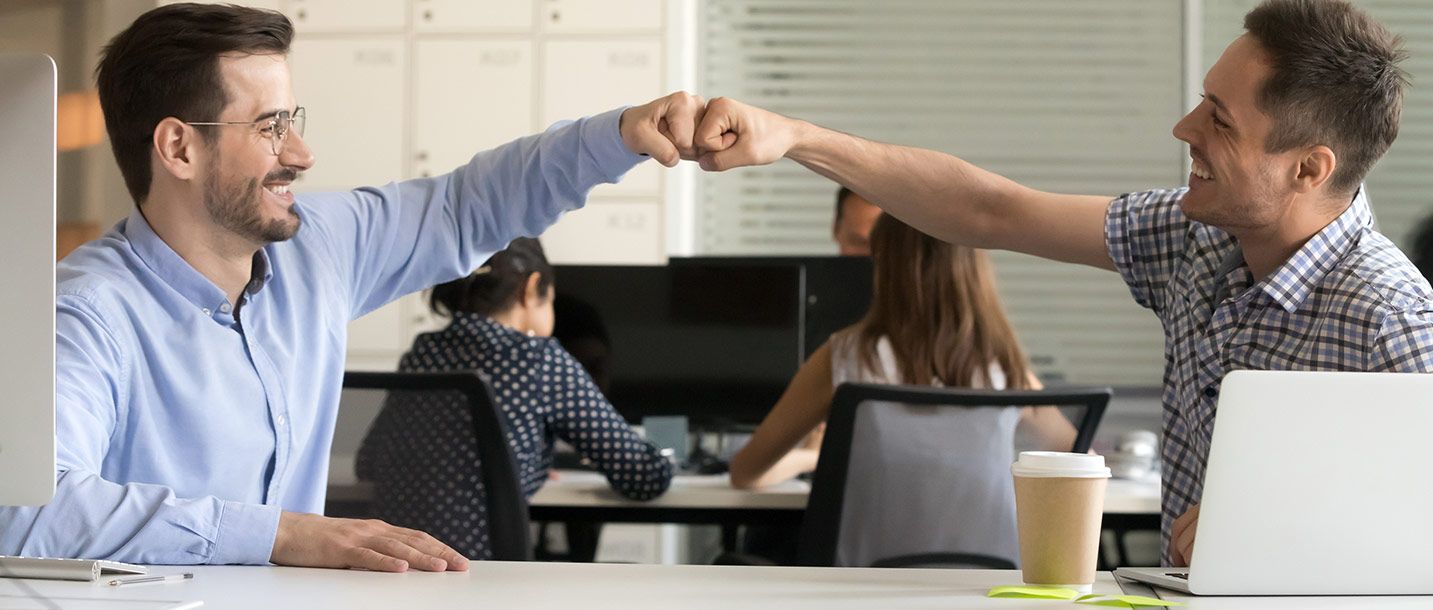 Zwei Männer im Büro machen einen Faustgruß.