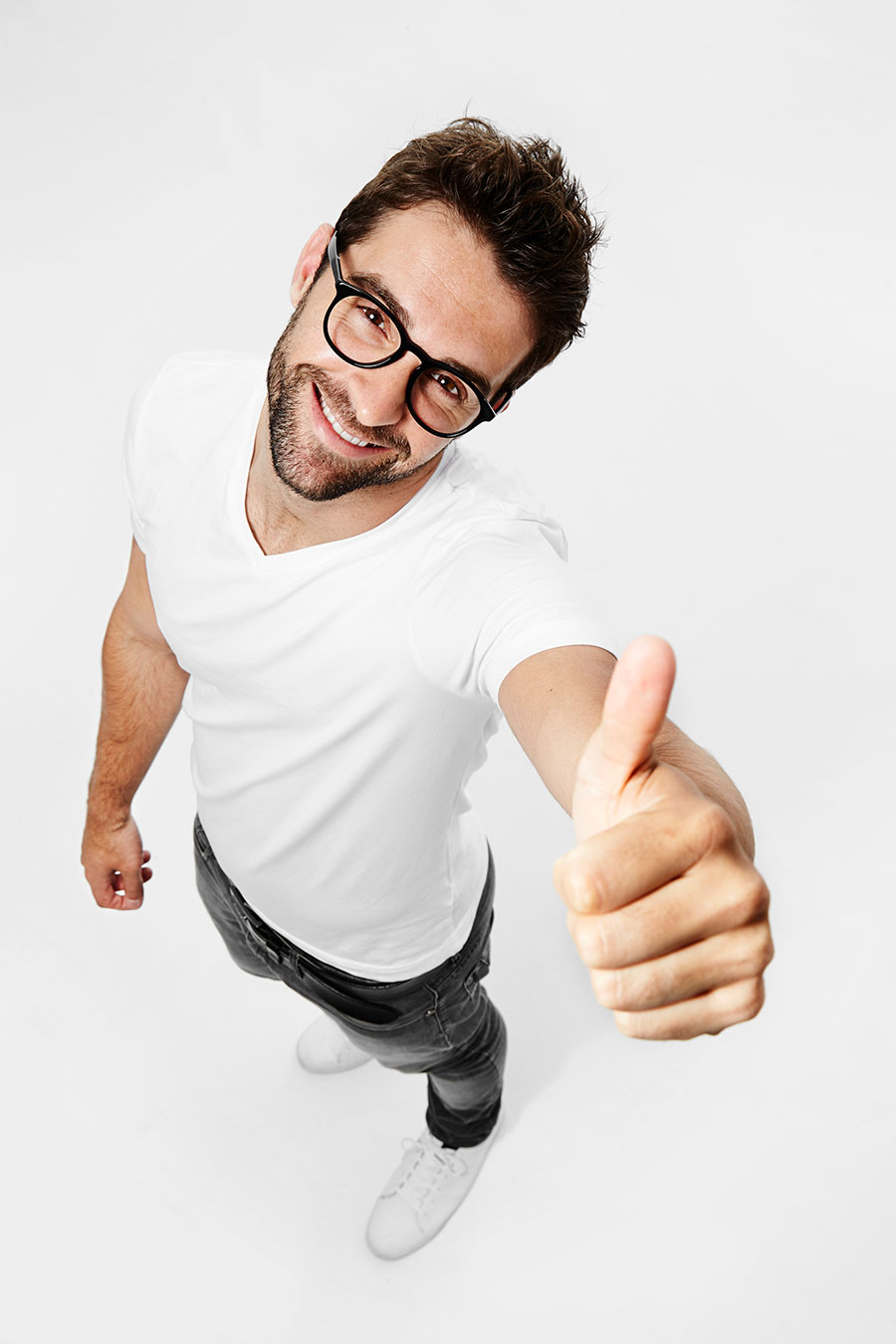 Lächelnder Mann mit Brille gibt Daumen hoch in einer Froschperspektive vor weißem Hintergrund